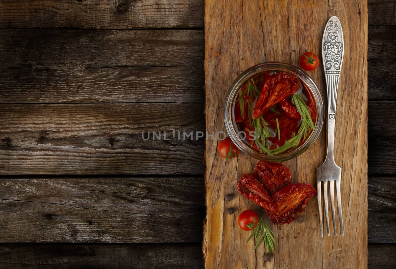 Delicious dried tomatoes in the jar of olive oil, the fork on wood background. In rustic style. With a space for text.