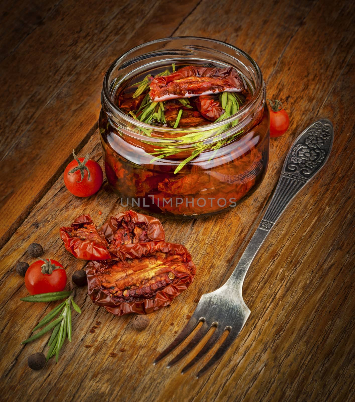 Delicious dried tomatoes in the jar of olive oil, the fork on wood background. In rustic style.