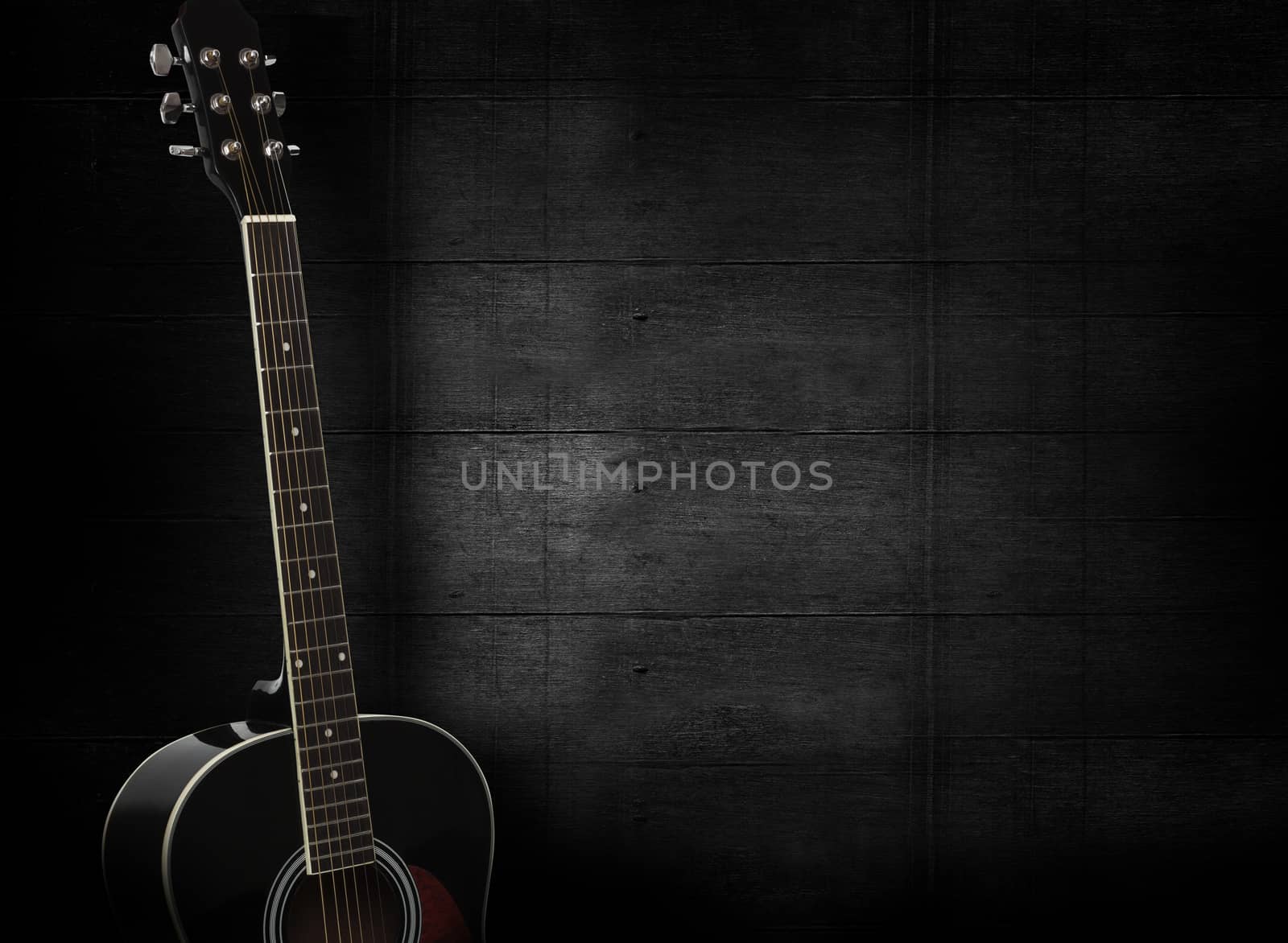 Black acoustic guitar on dark black wooden background.