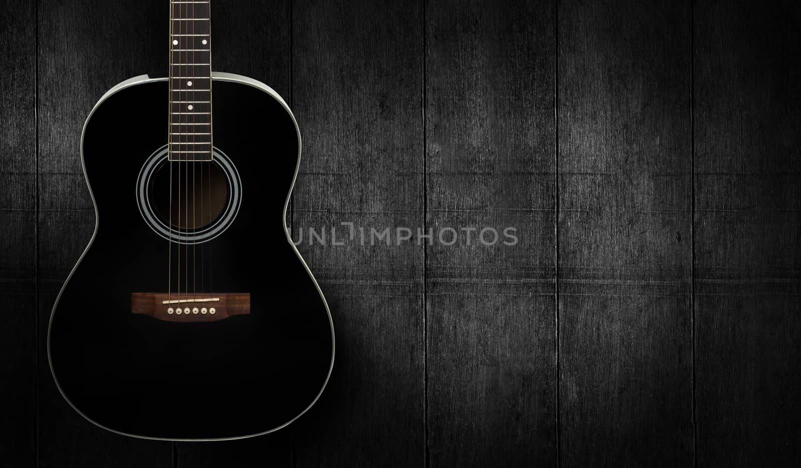 Black acoustic guitar on dark black wooden background.