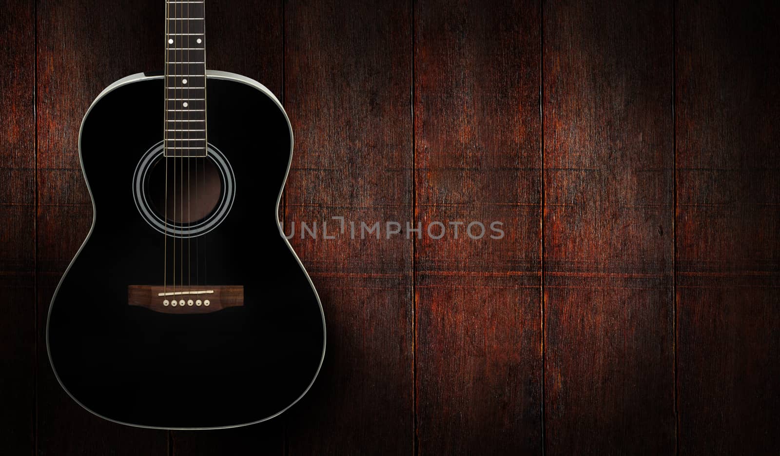 Black acoustic guitar on dark red wooden background.