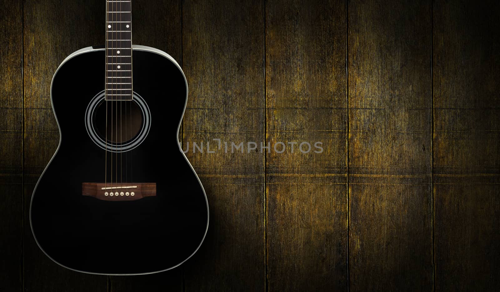 Black acoustic guitar on dark yello wooden background.