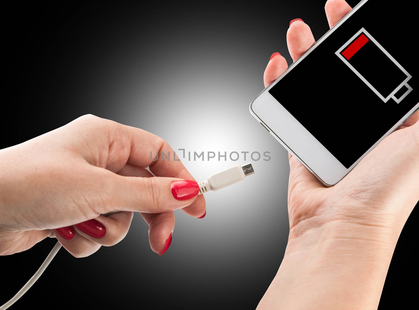Female hand holding low battery smartphone and connect charger isolated on black background