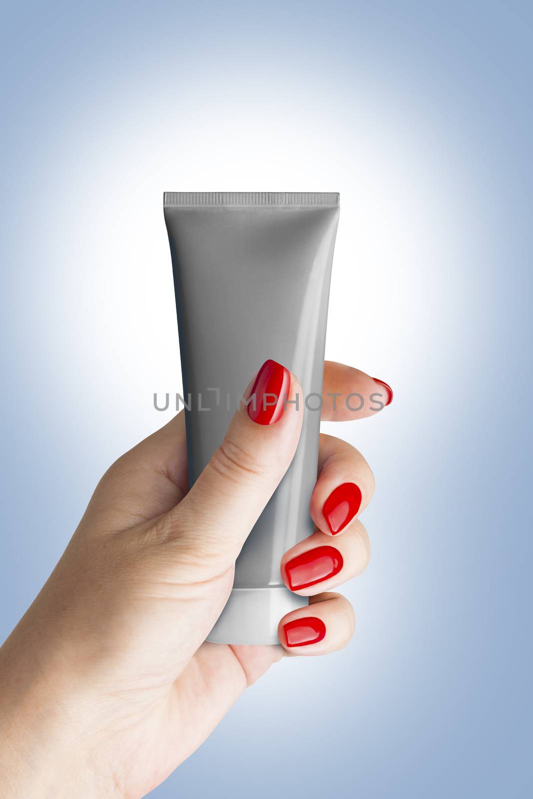 Plastic tube for cosmetics and body care in a female hand, isolated. Isolated on blue background. With clipping path