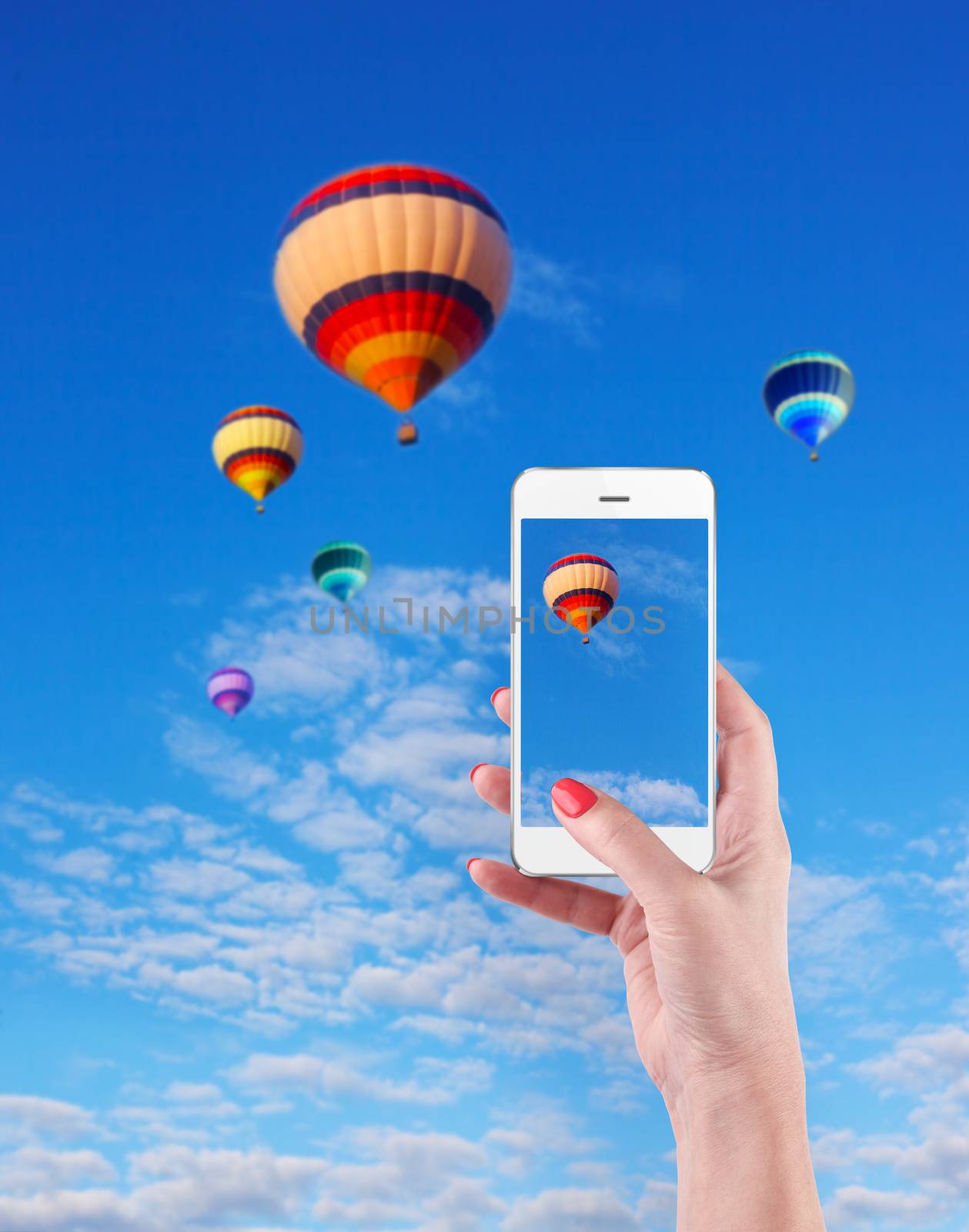 Female Hands Holding Smart Phone Displaying Photo of Blue Sky with Hot Air Balloons Behind.