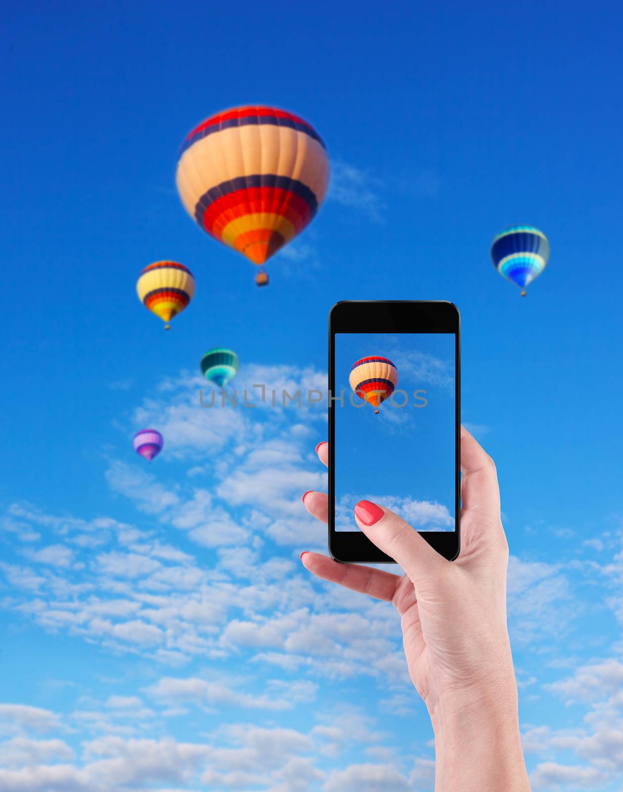 Female Hands Holding Smart Phone Displaying Photo of Blue Sky with Hot Air Balloons Behind.