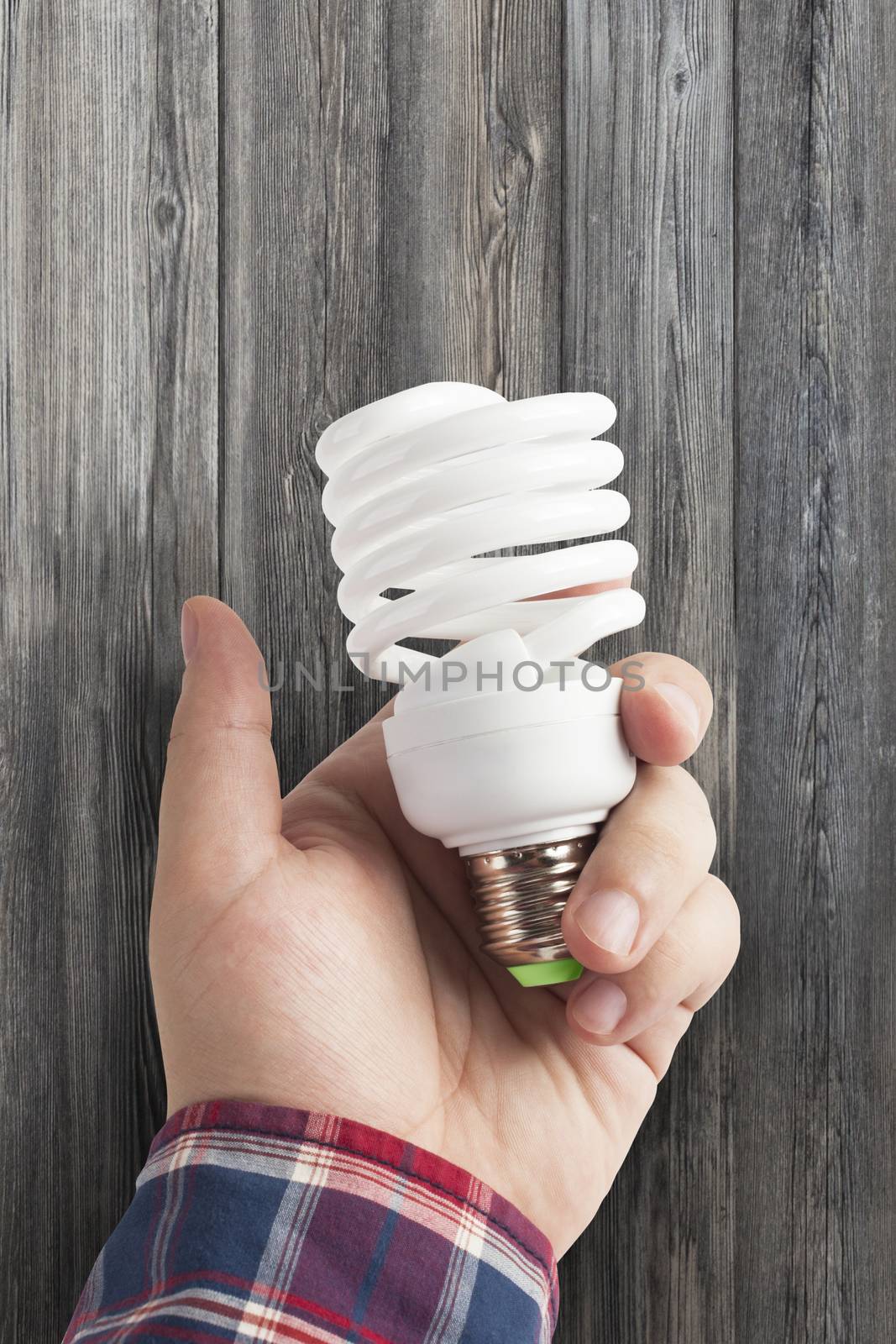 Energy saving lamp in the man's hand on dark wood background closeup. With clipping path