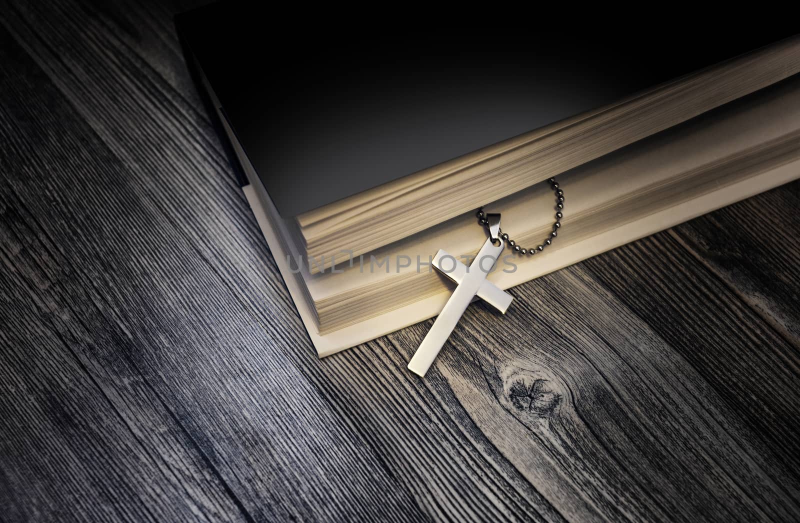 Metal cross on top of a black book cover on wooden background