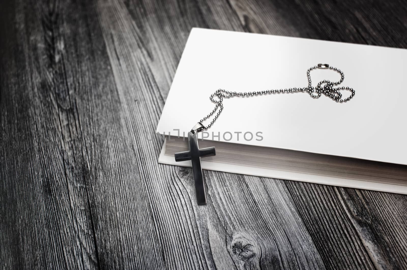 Metal cross on top of a white book cover on wooden background