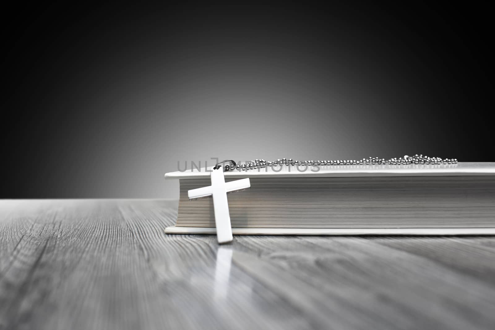 Metal, religious Christian cross with a book on a wooden background close up.