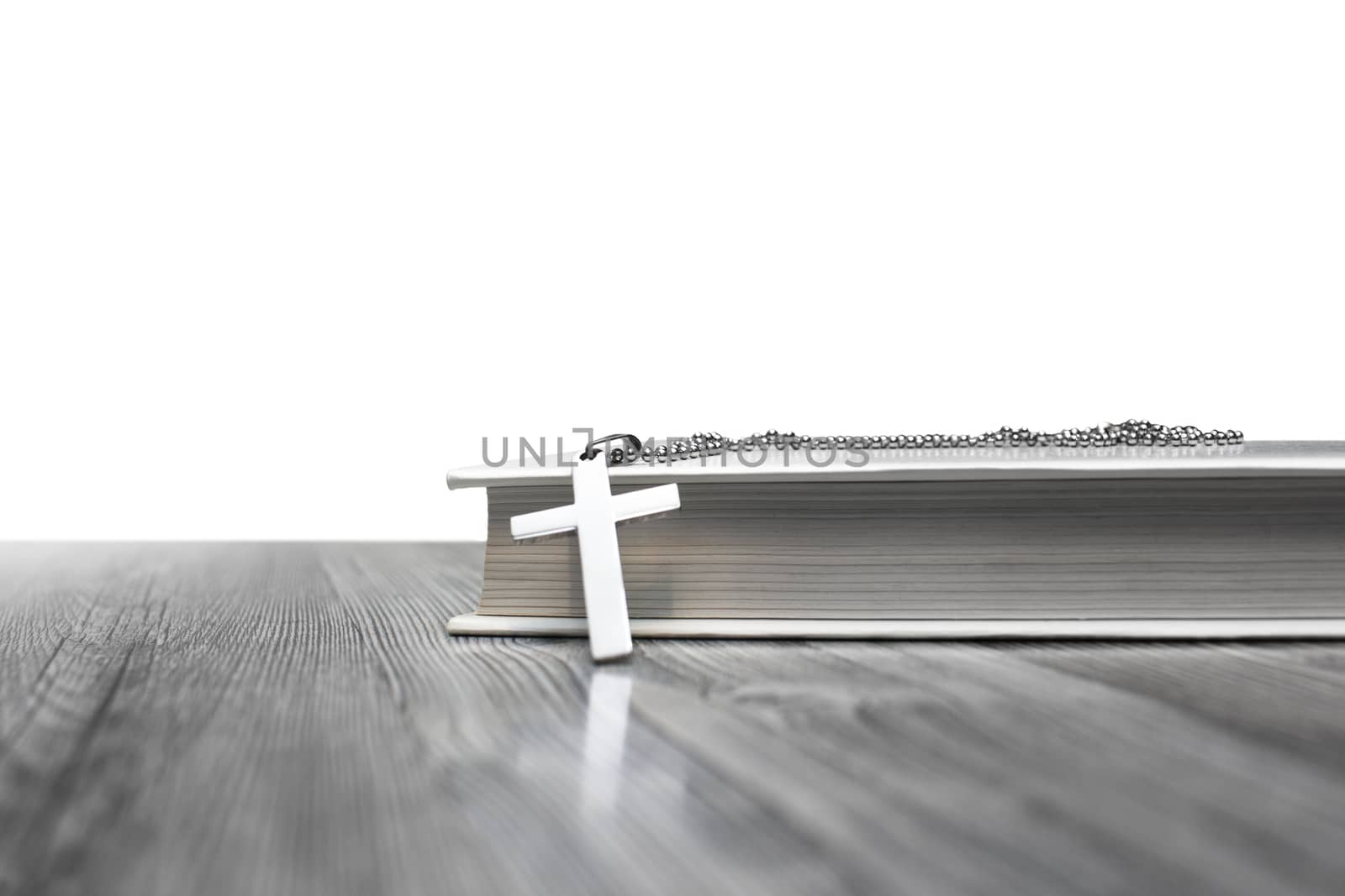 Metal cross on top of a white book cover on wooden background