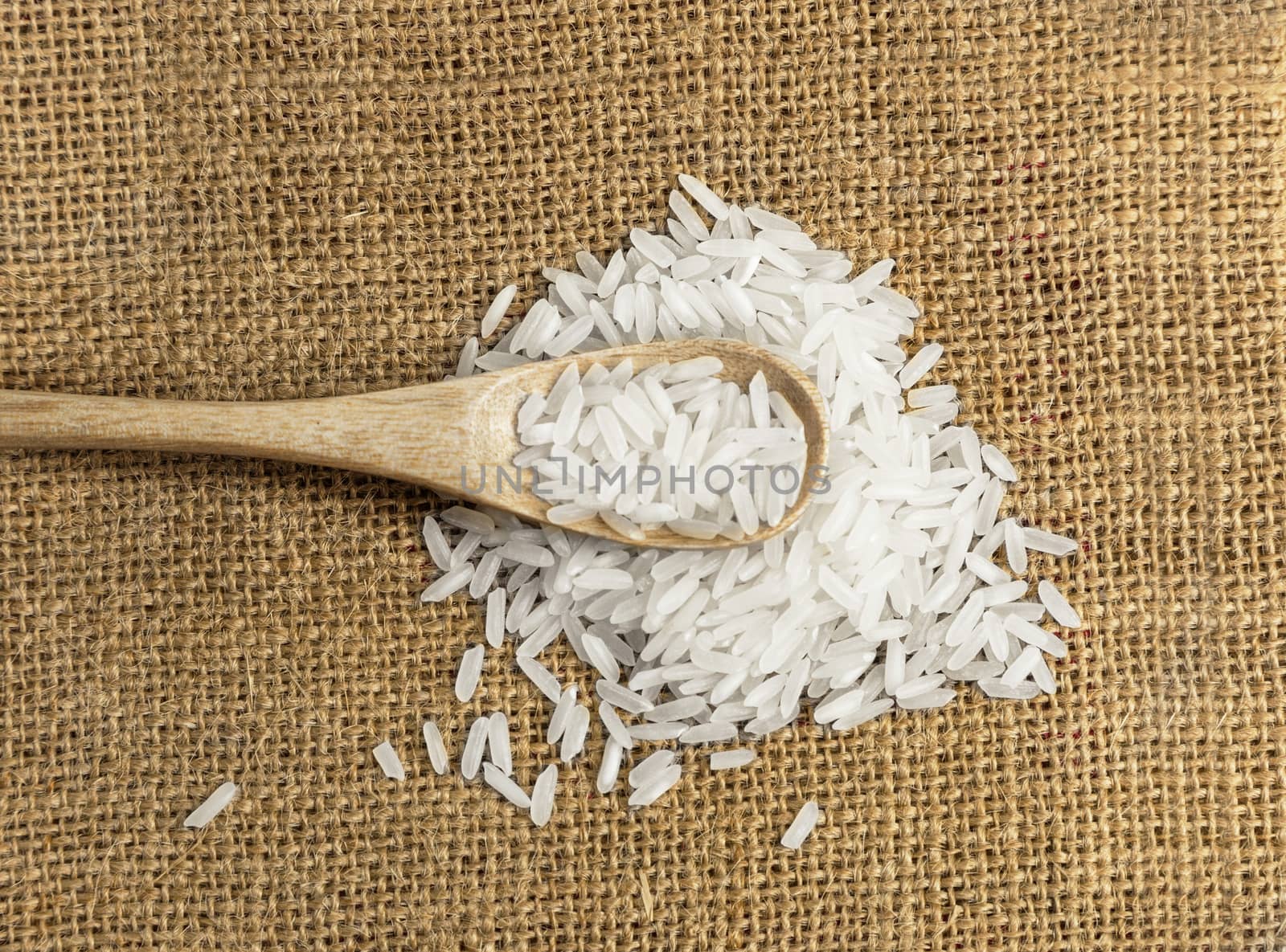 Asian uncooked white rice in a wooden spoon on a background of rough cloth
