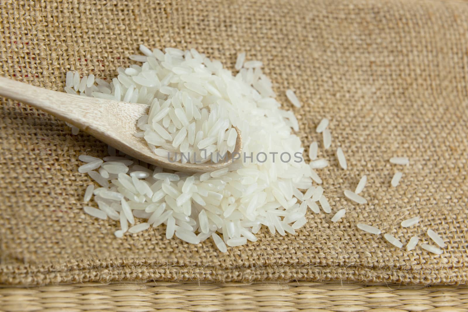 Asian uncooked white rice in a wooden spoon on a background of rough cloth