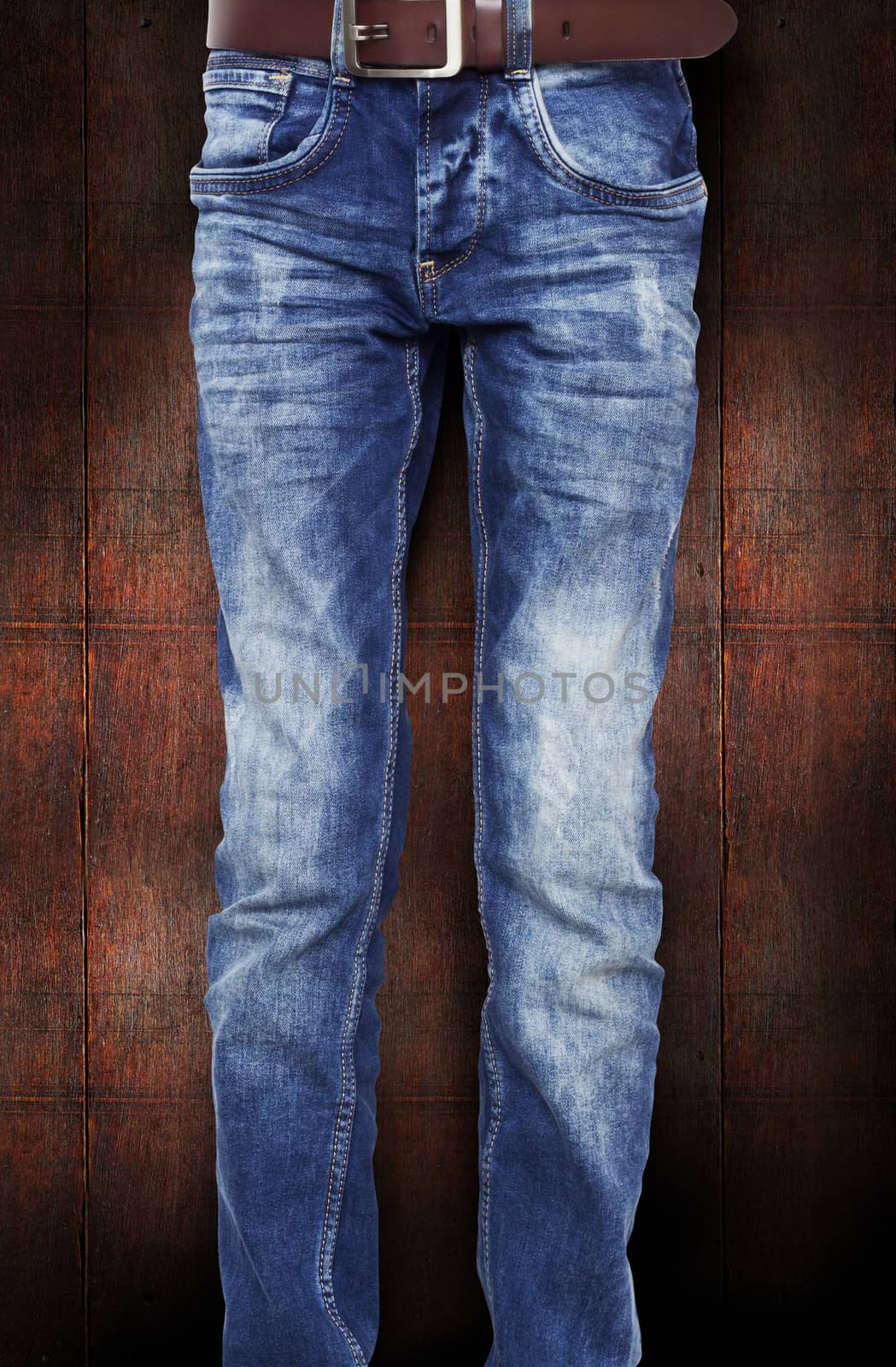 Blue jeans for the teenager with a belt. On a dark red background wood texture. With clipping path