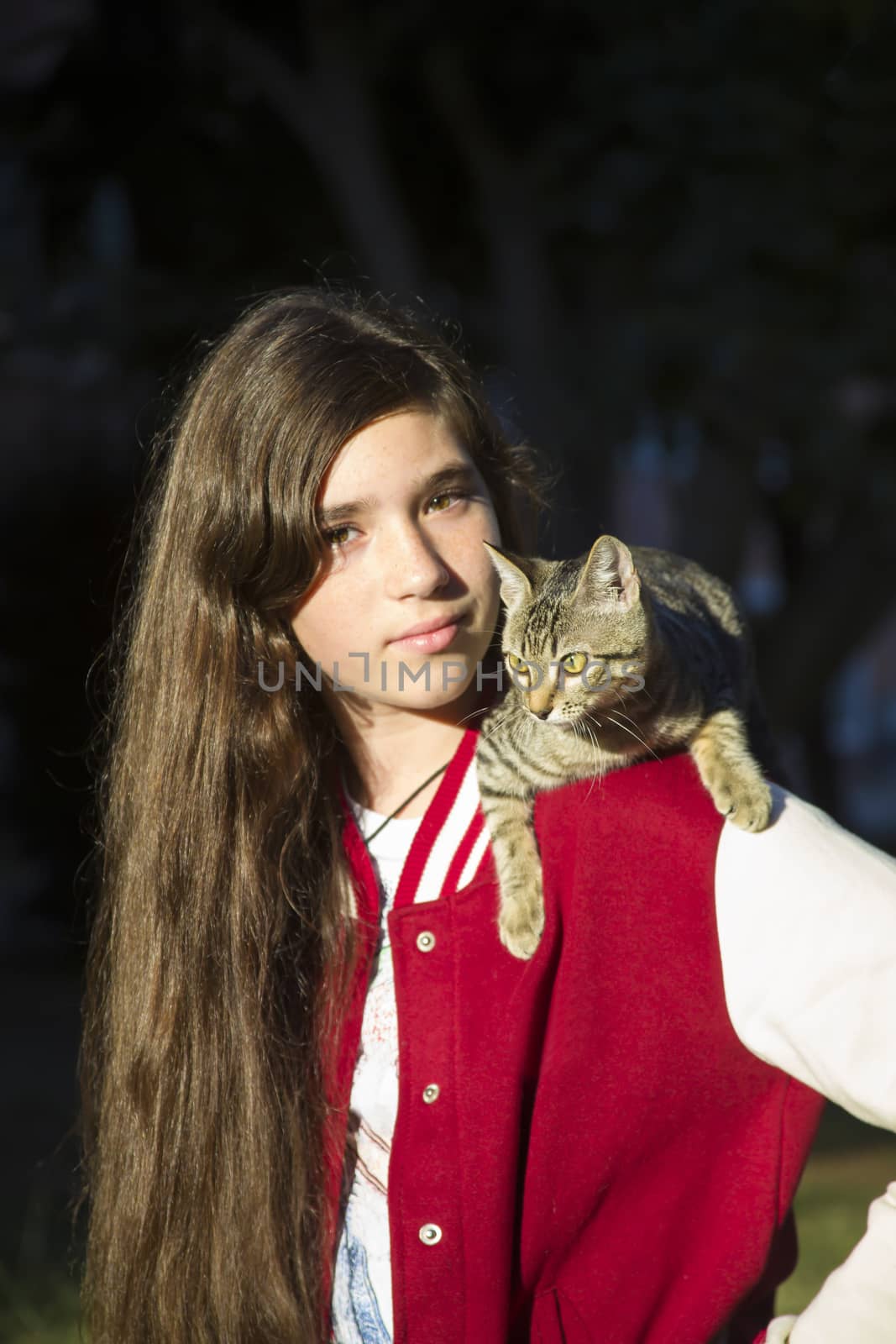Autumn sunny photo of teenage girl close-up, with a cat sitting on her shoulder, street photo on dark background.