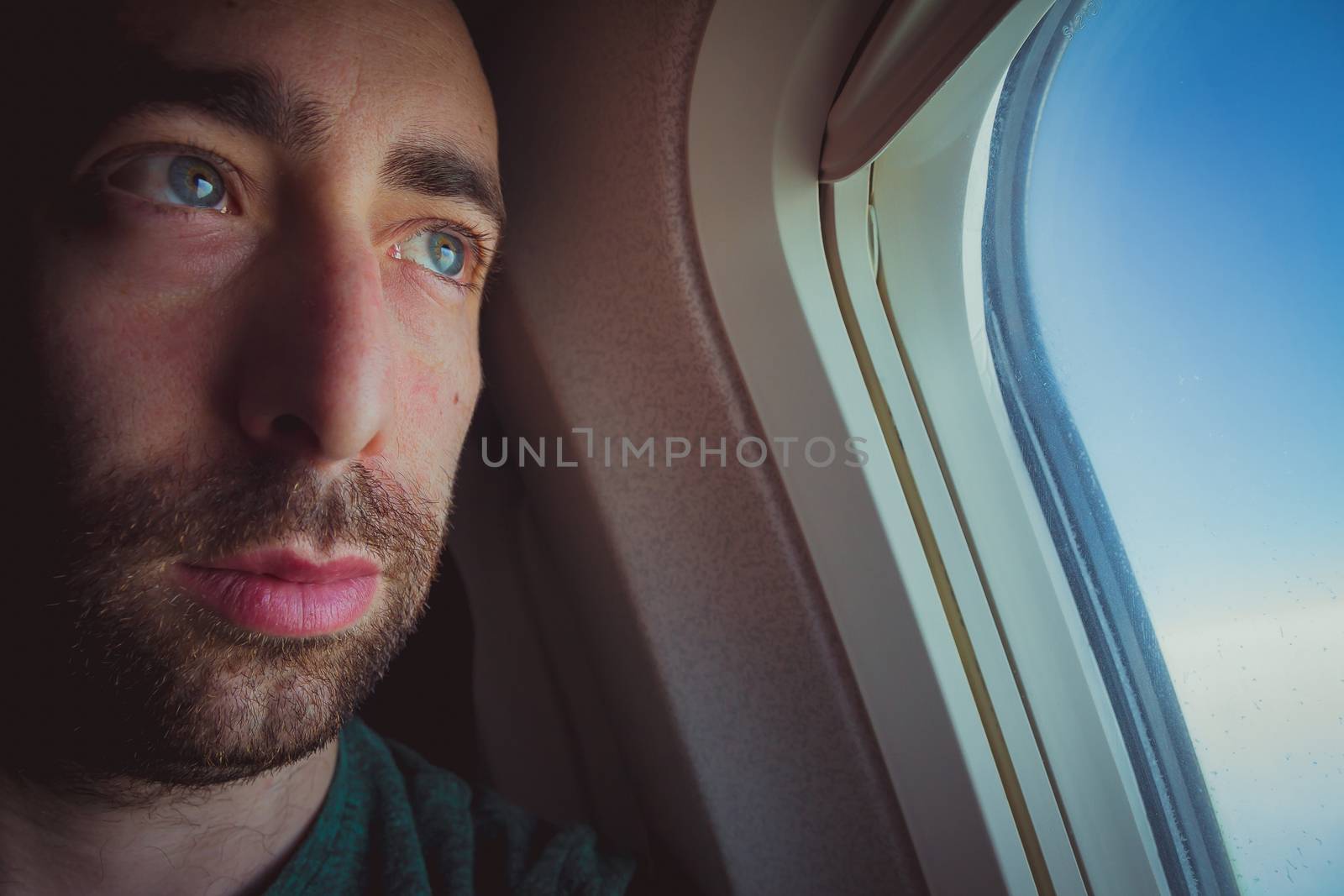 Close up of a pensive man looking outside through the window of an airplane.