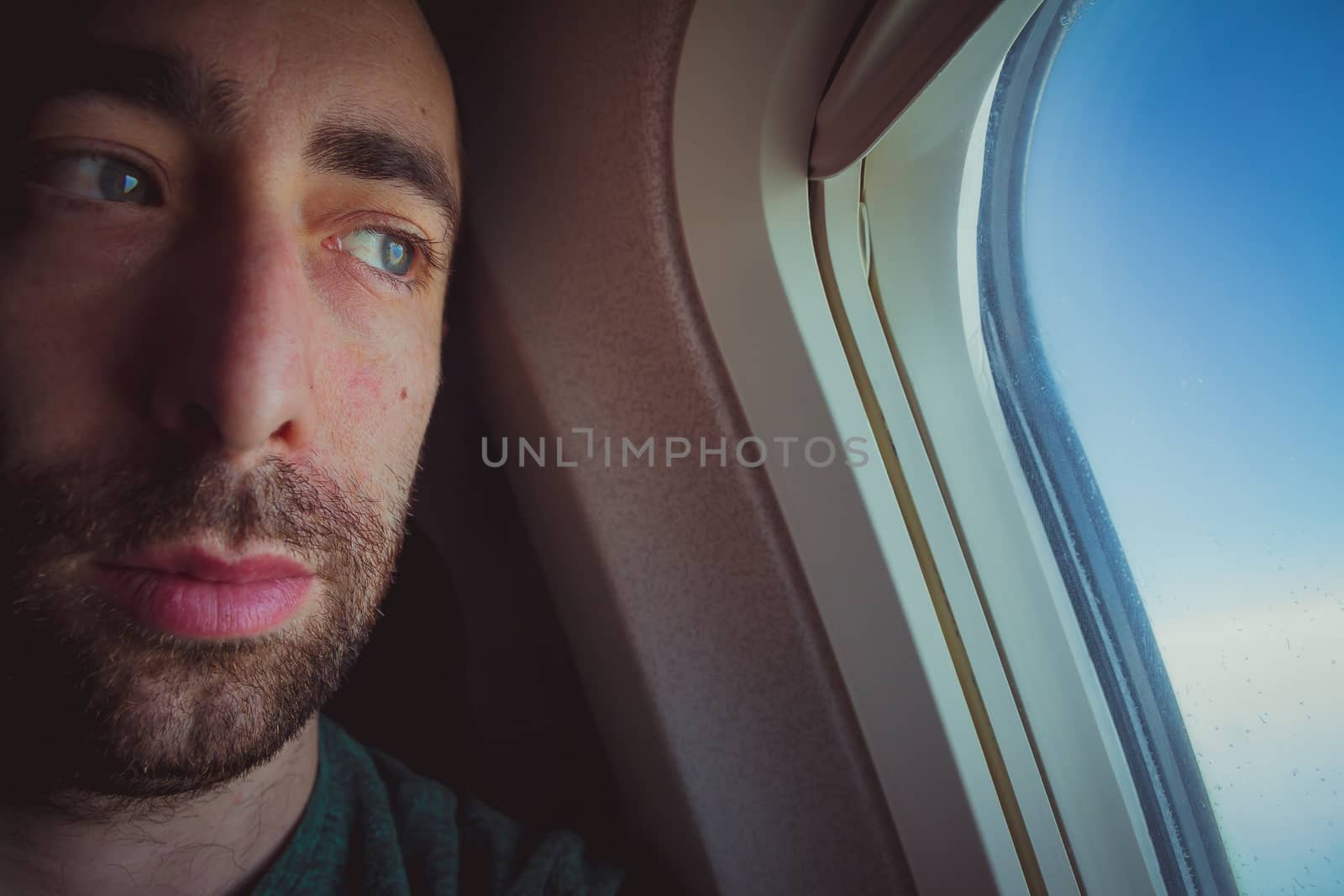 Close up of a pensive man looking outside through the window of an airplane.