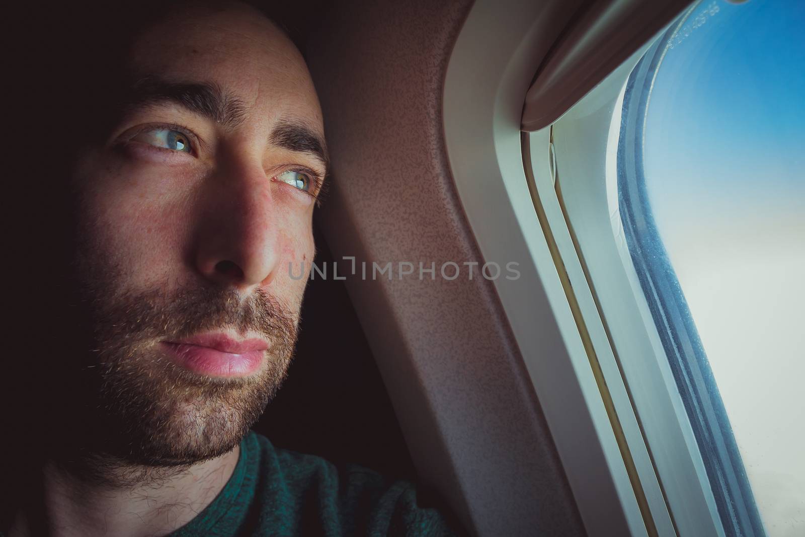 Close up of a pensive man looking outside through the window of an airplane.