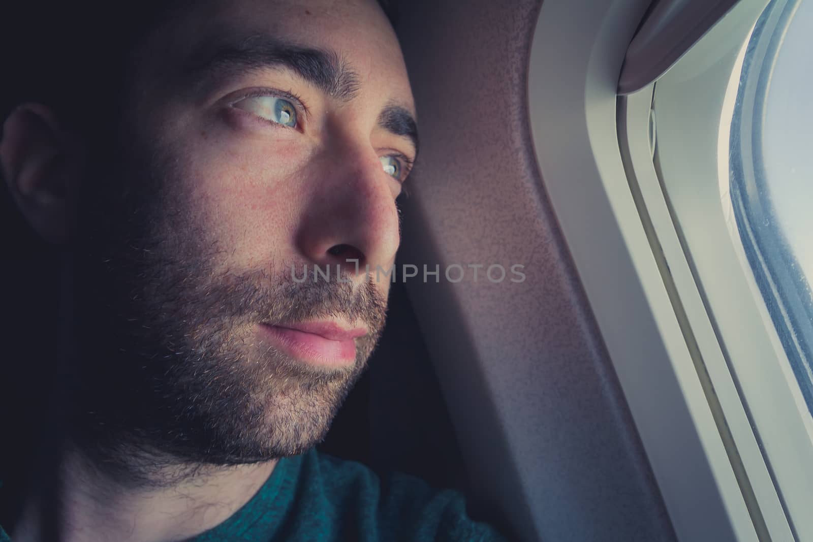 Close up of a pensive man looking outside through the window of an airplane.
