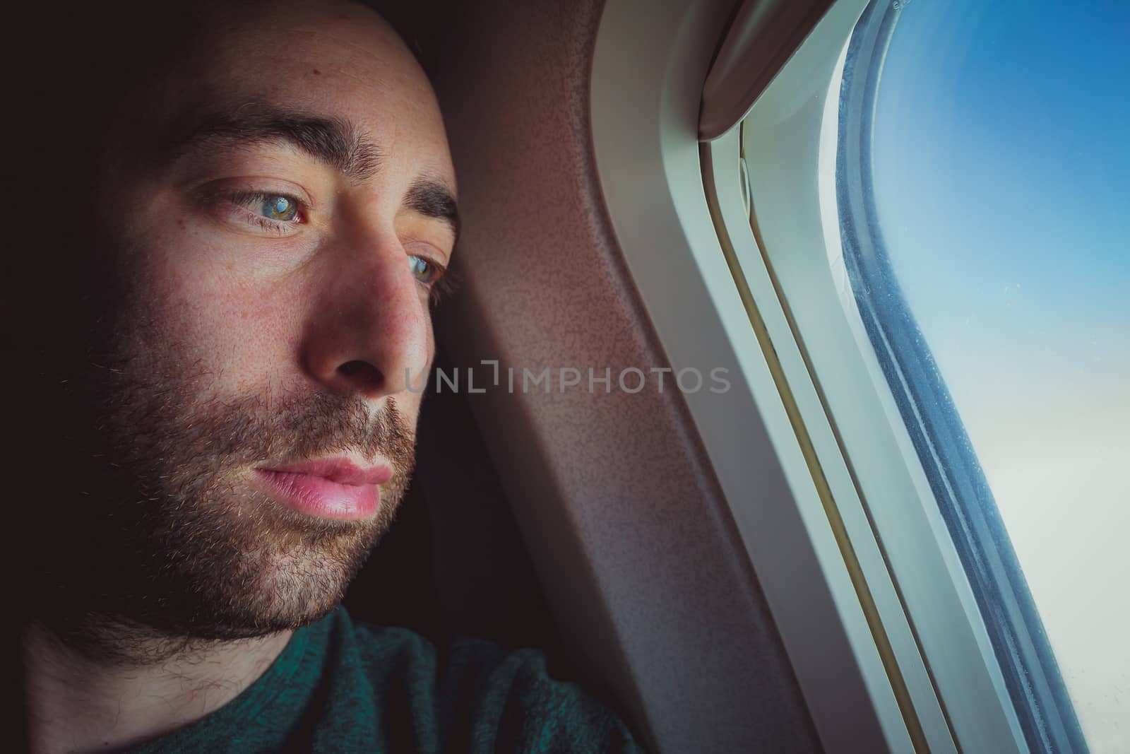 Close up of a pensive man looking outside through the window of an airplane.