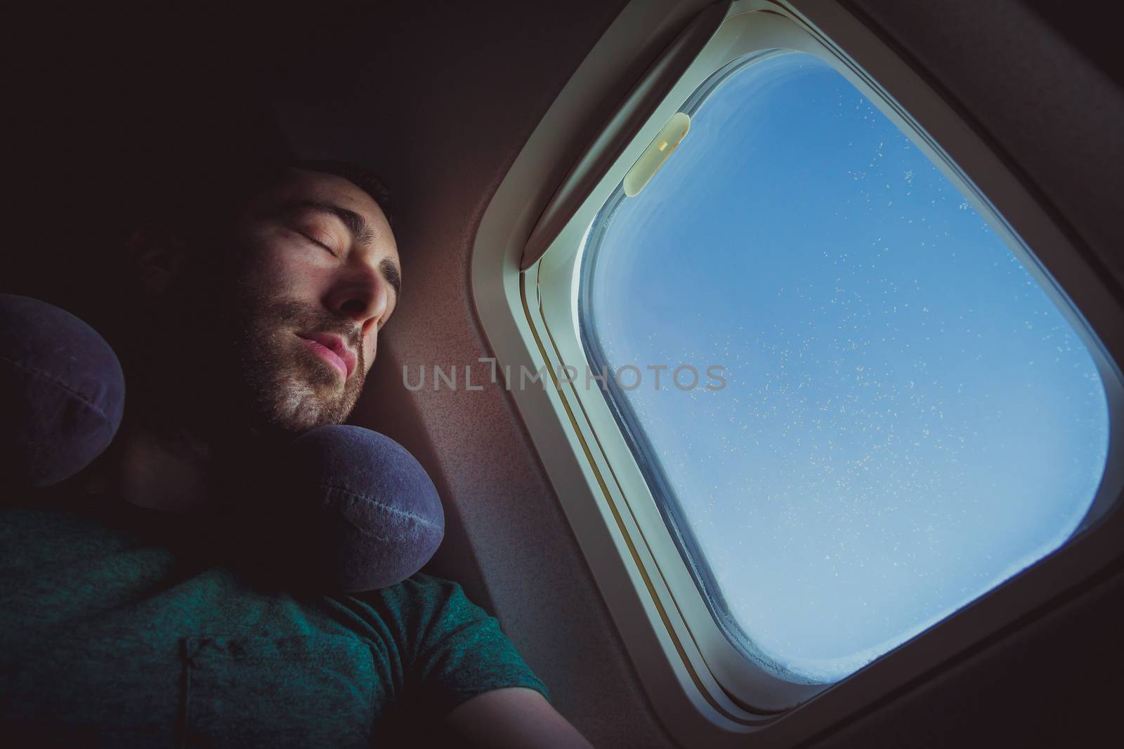 Young man with neck pillow resting and sleeping on an airplane.
