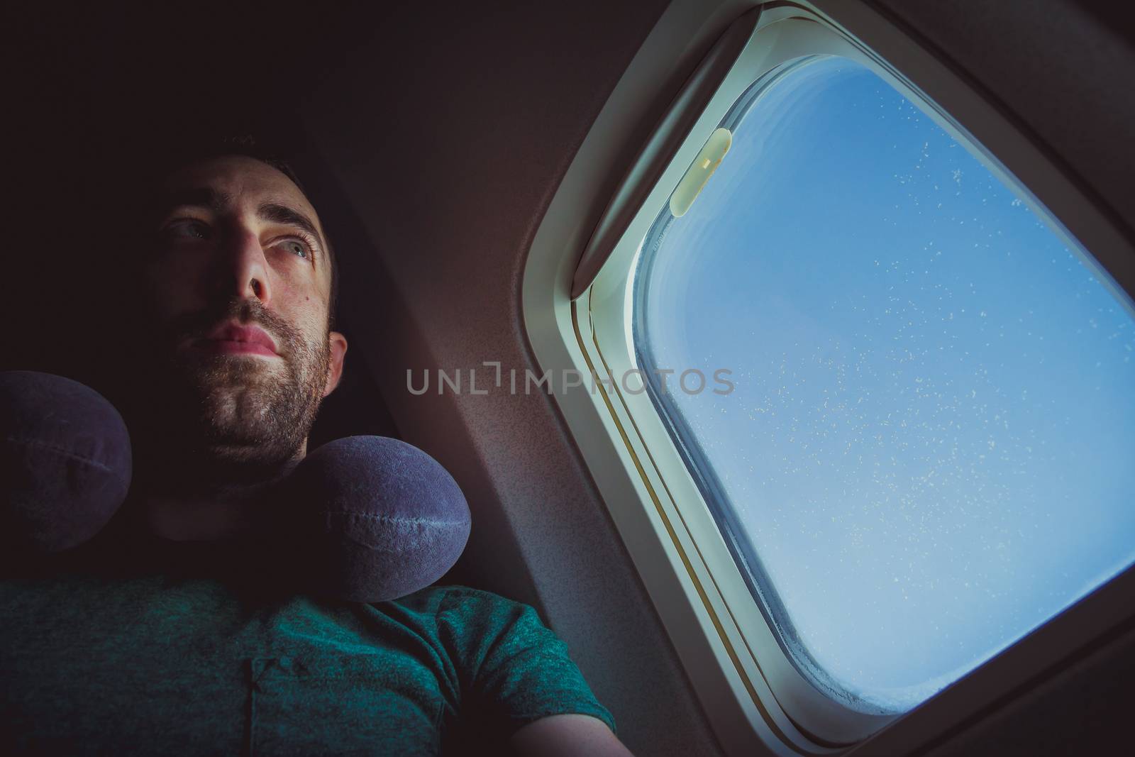 Pensive man with neck pillow seat by the window of an airplane.