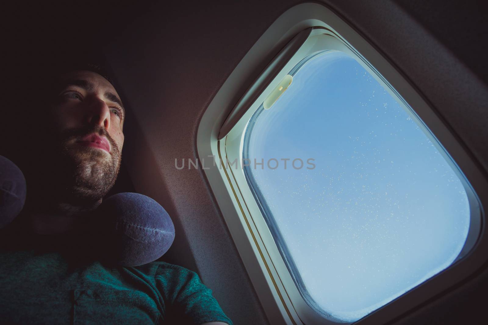 Pensive man with neck pillow seat by the window of an airplane by wavemovies