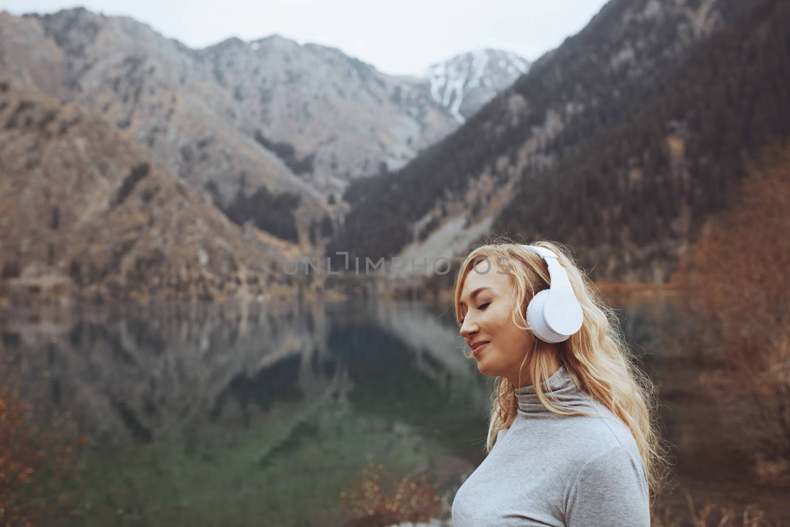 Woman wearing wireless headphones at the mountain lake by Novic