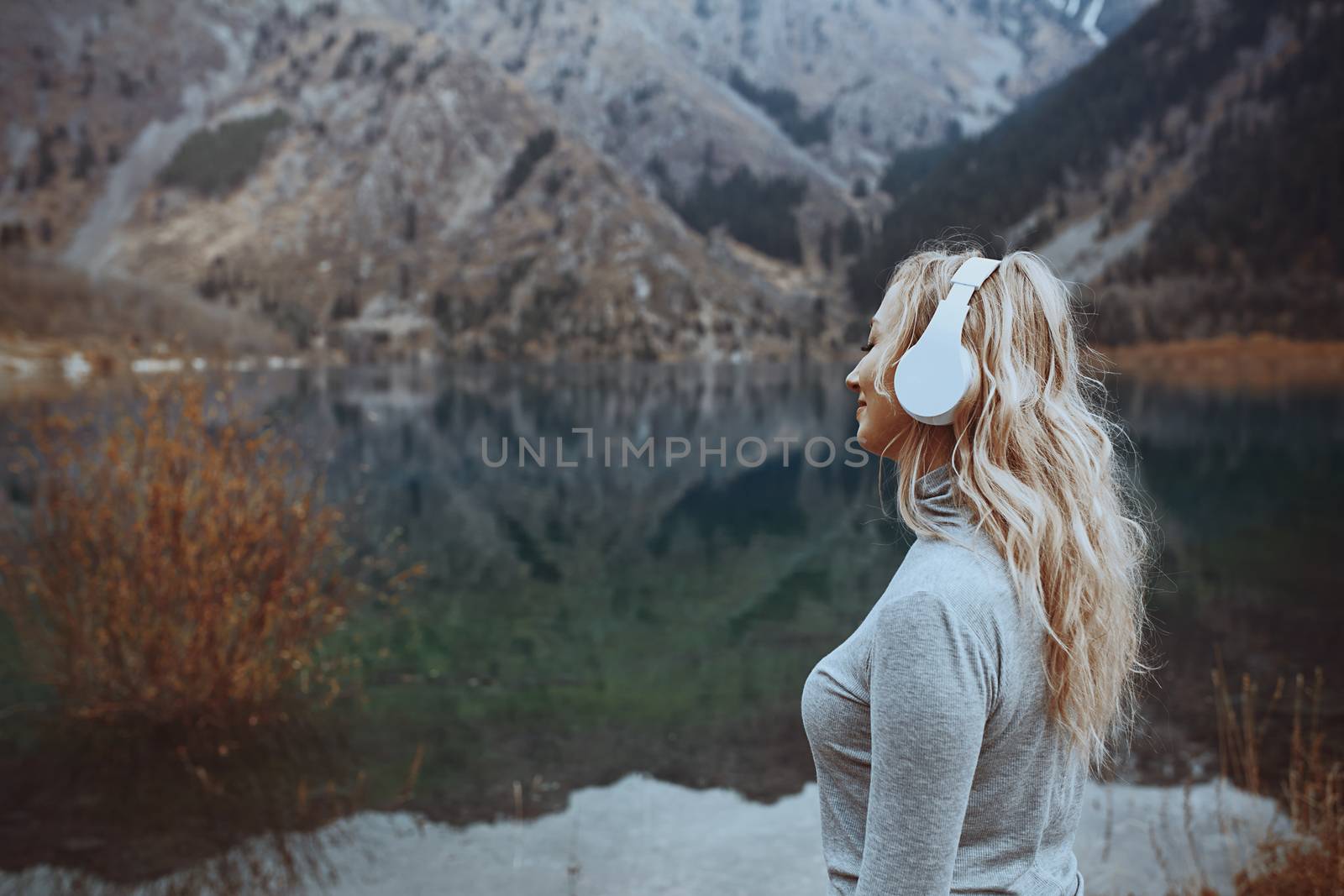 Woman wearing wireless headphones at the mountain lake by Novic