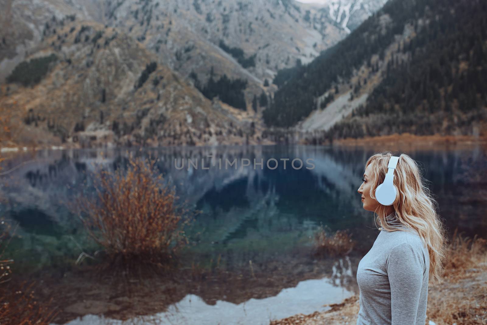 Woman wearing wireless headphones at the mountain lake by Novic