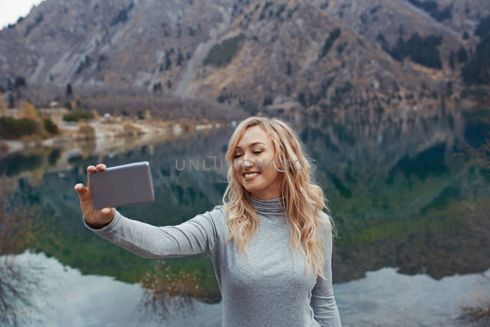 Smiling woman makes selfie at the mountain lake