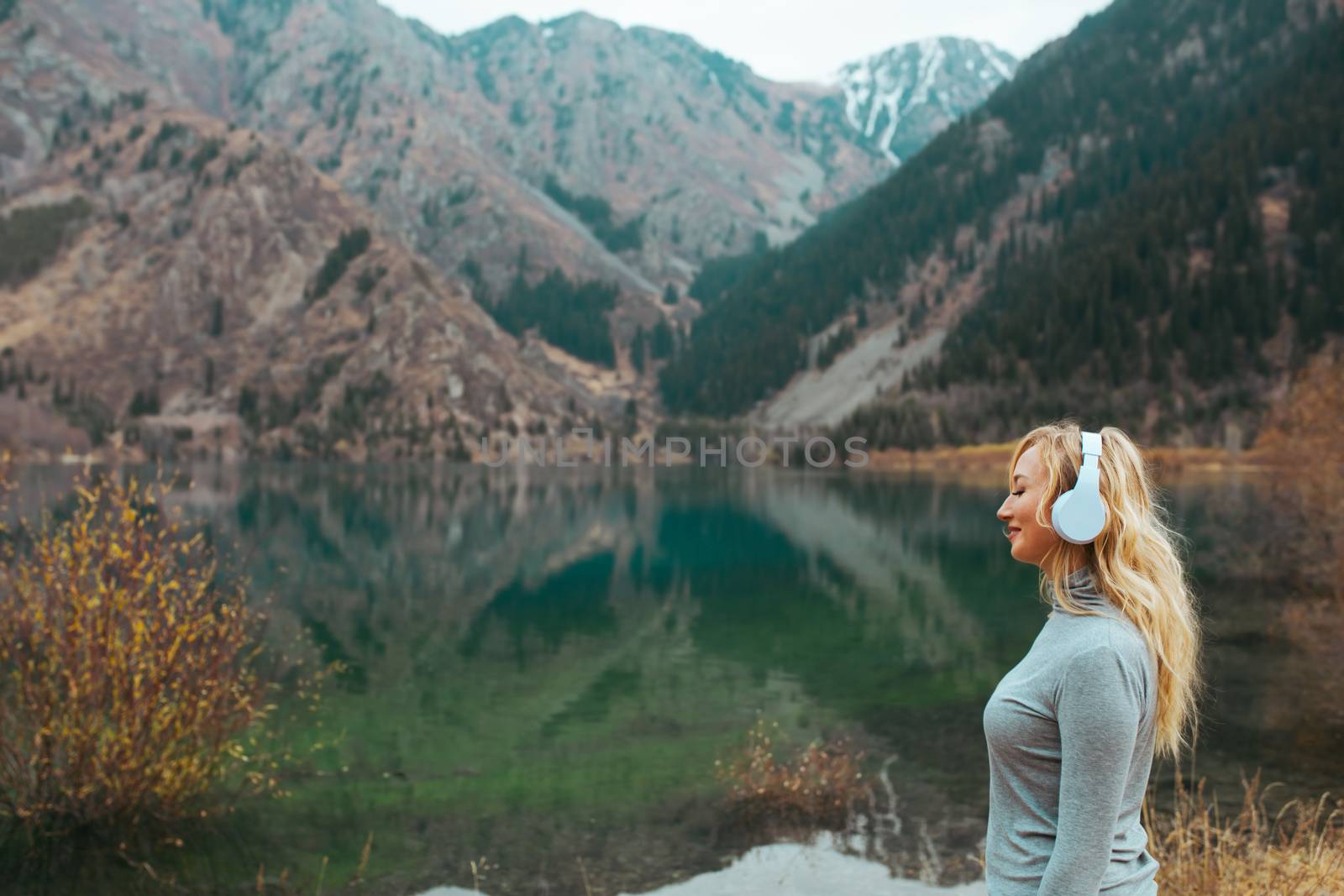 Woman wearing wireless headphones at the mountain lake