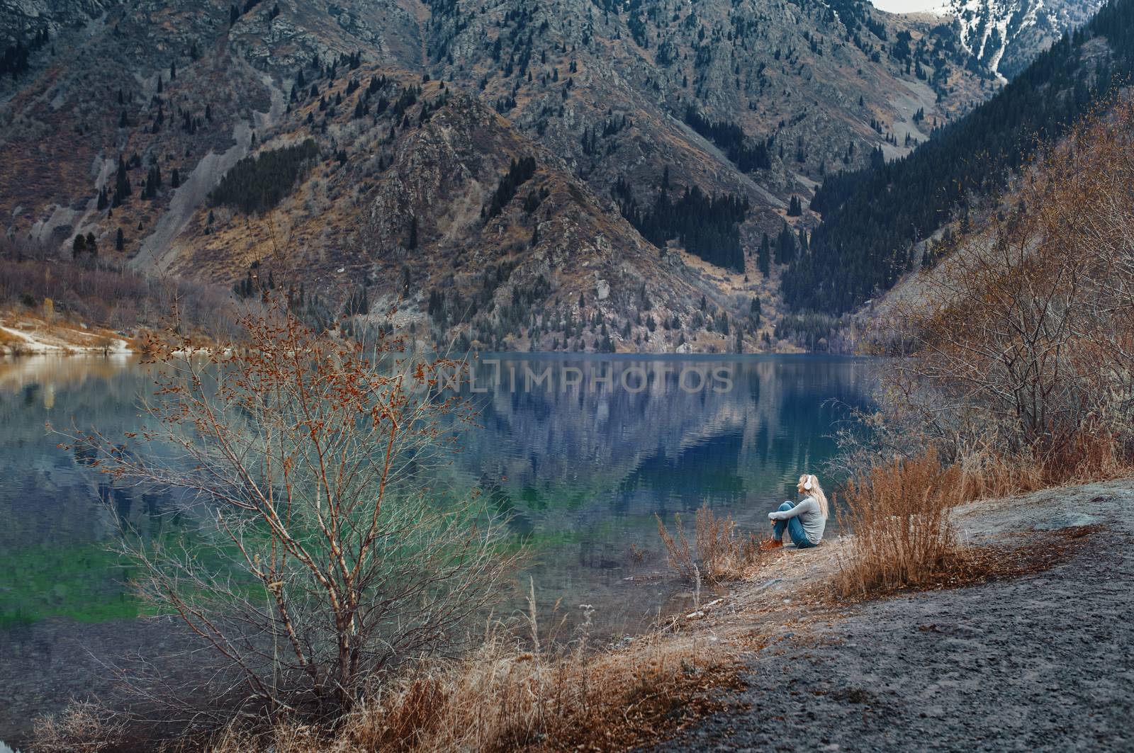 Woman listening music at the water's edge of mountain lake by Novic