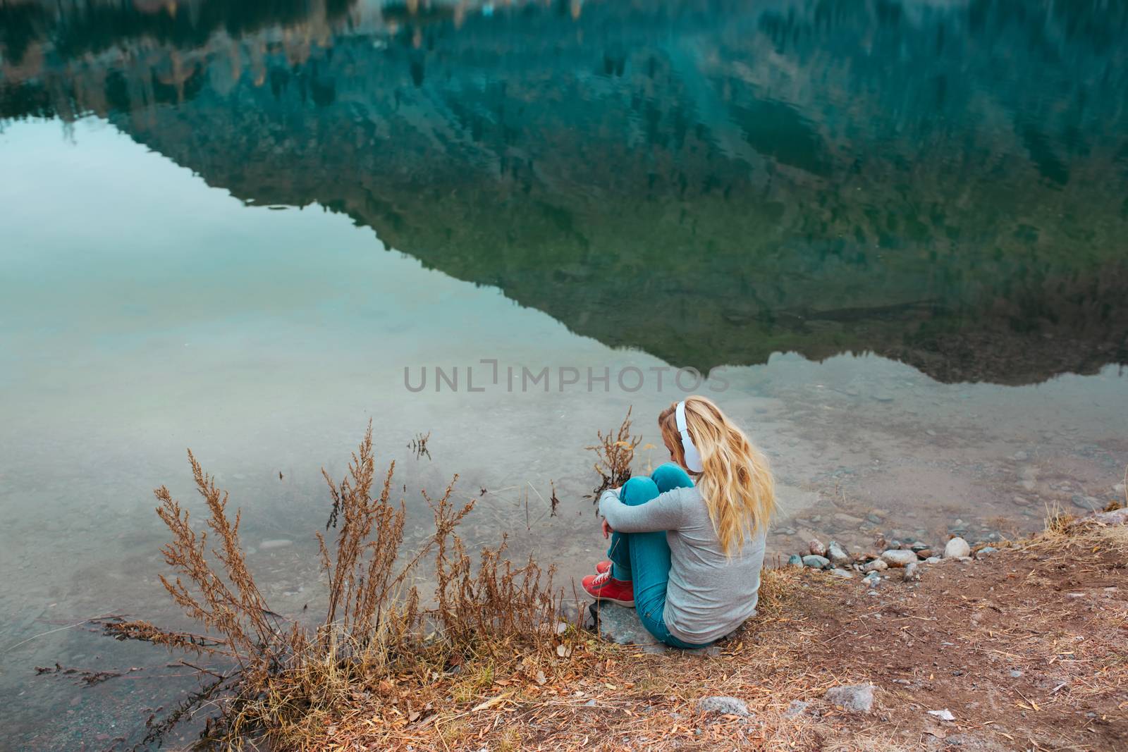 Woman listening music at the water's edge of mountain lake by Novic