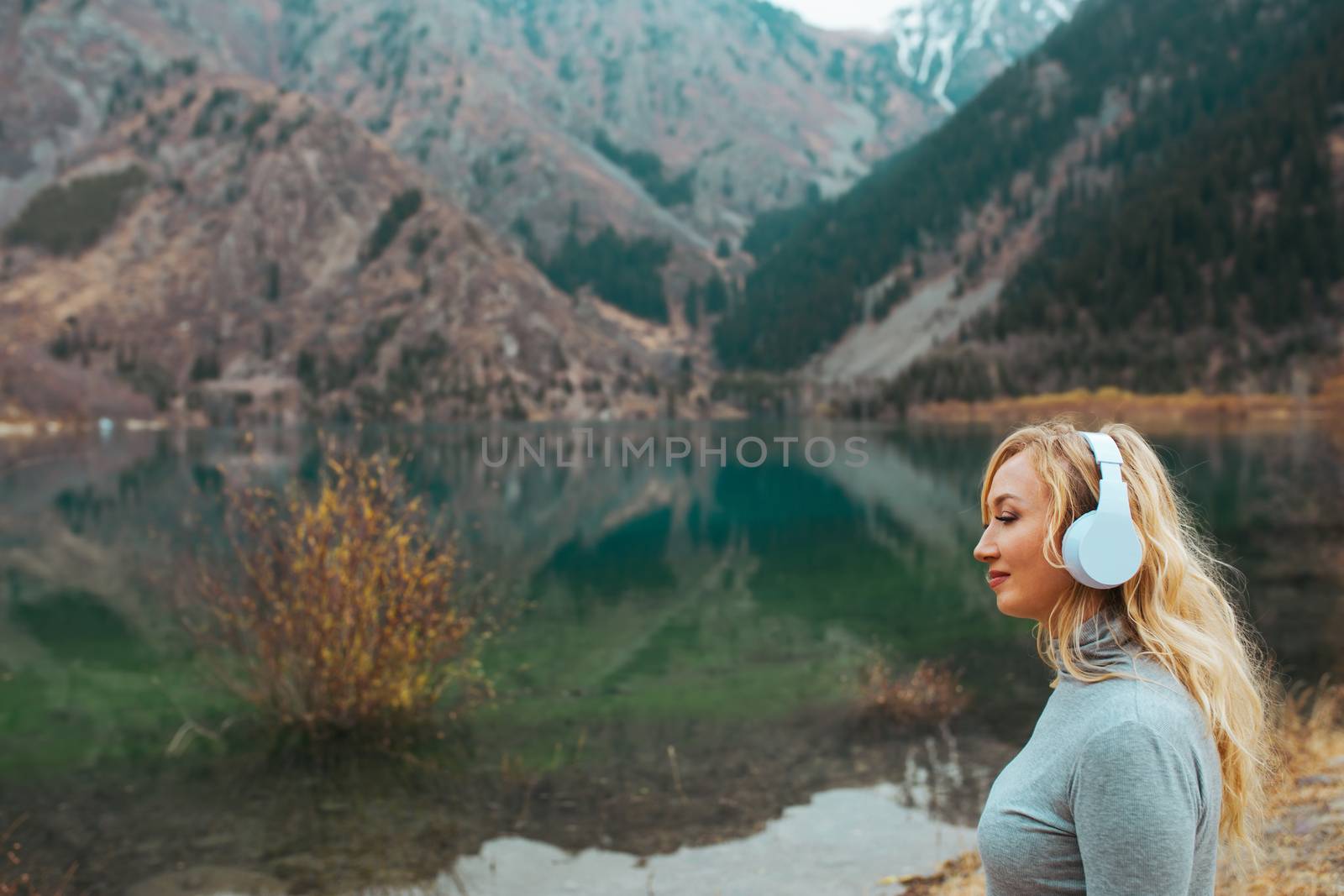 Woman wearing wireless headphones at the mountain lake by Novic