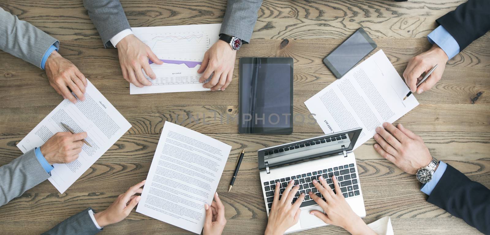 Business team working with contract, financial reports and laptop dicussing deal sitting around office table