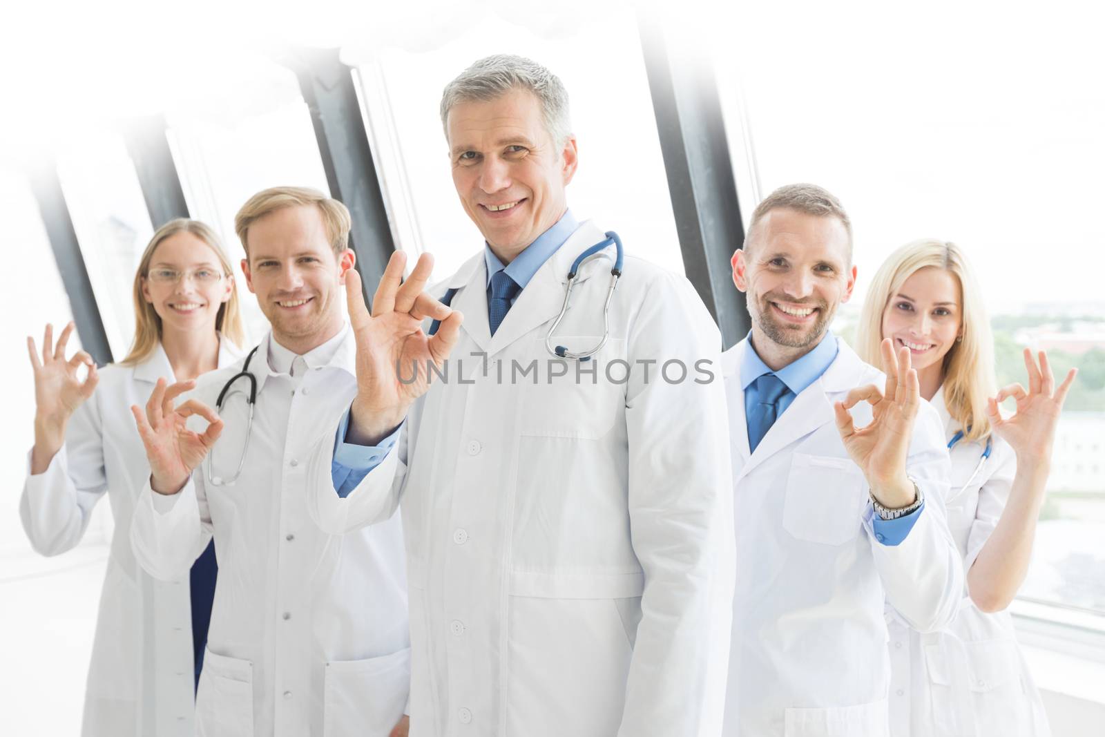 Successful team of medical doctors are looking at camera and showing ok sign