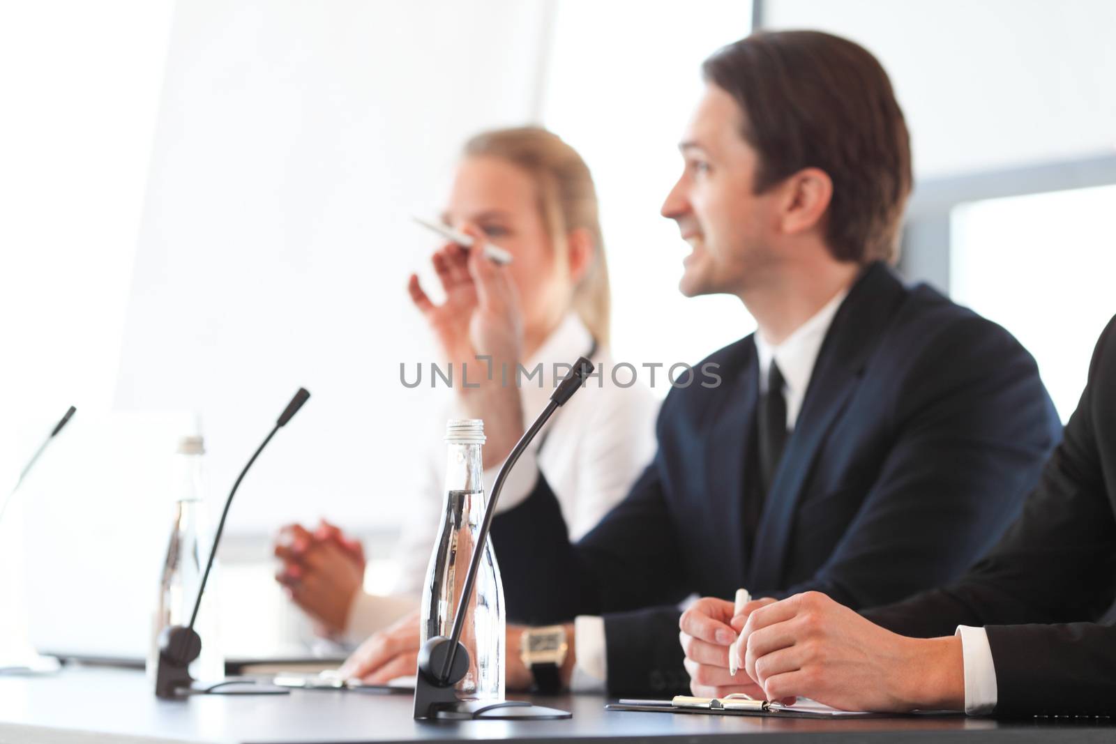 Group of speakers at business meeting at the table with microphones