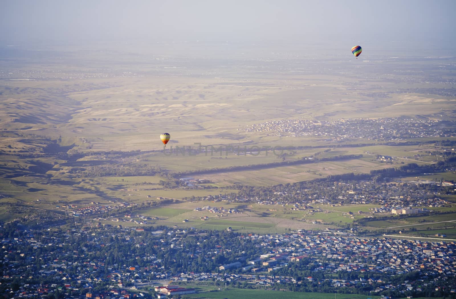 Hot air balloons above the green field and villages by Novic