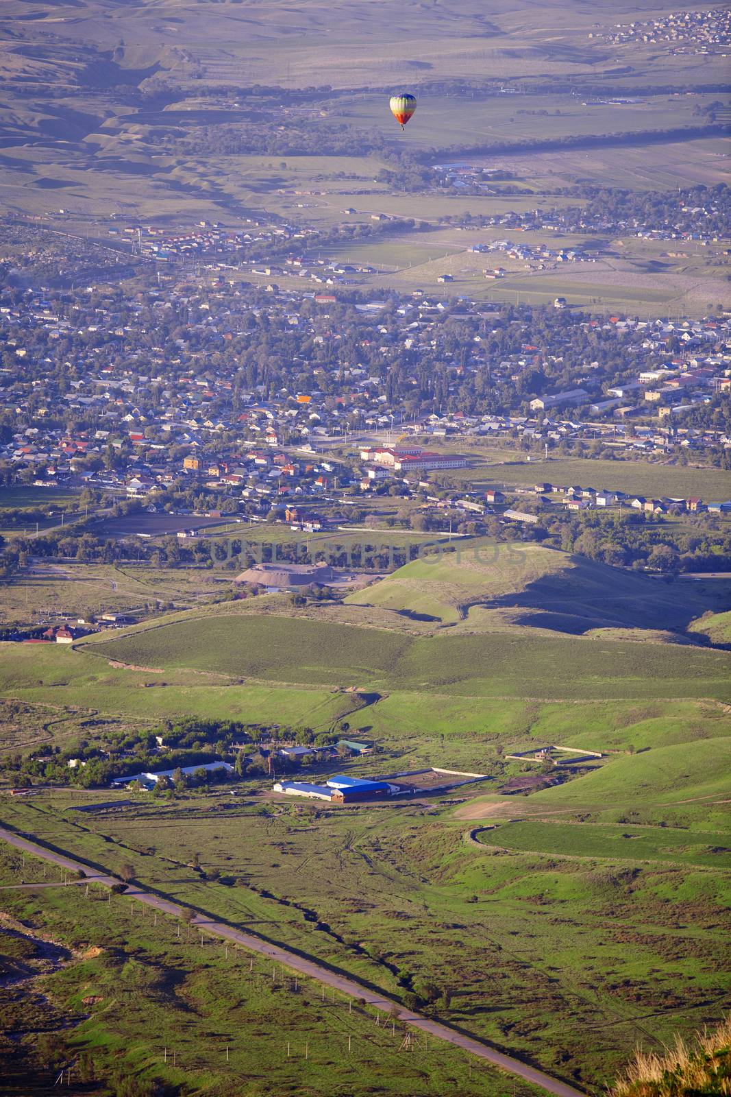 Hot air balloon above the green field and villages by Novic