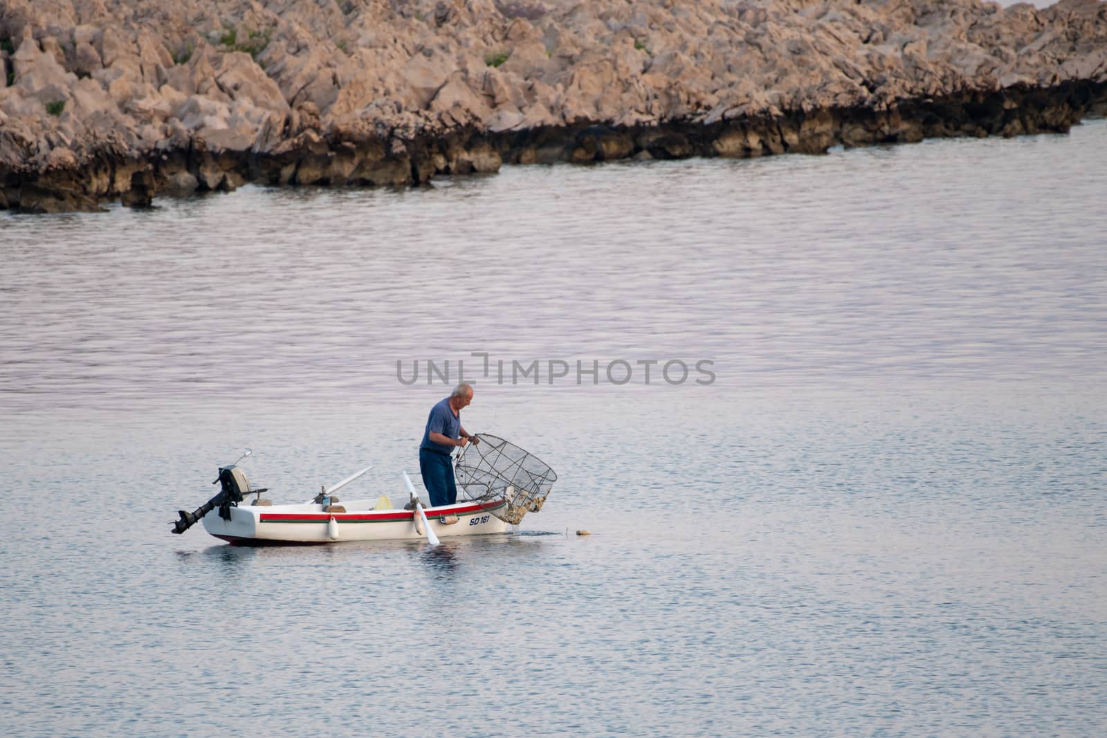 Old traditional fisherman in Croatia on a small wooden boat catching fish with fishing cage, pod by asafaric