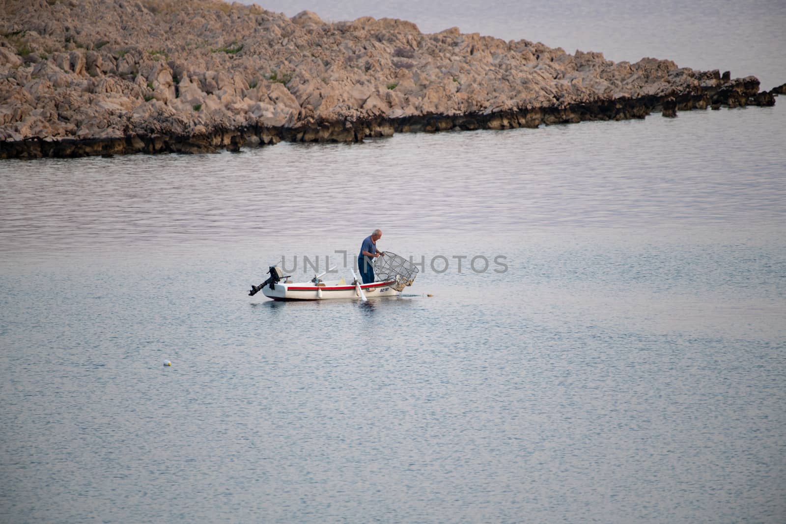 Old traditional fisherman in Croatia on a small wooden boat catching fish with fishing cage, pod, the catch is small due overfishing and makes a hard living the traditional way