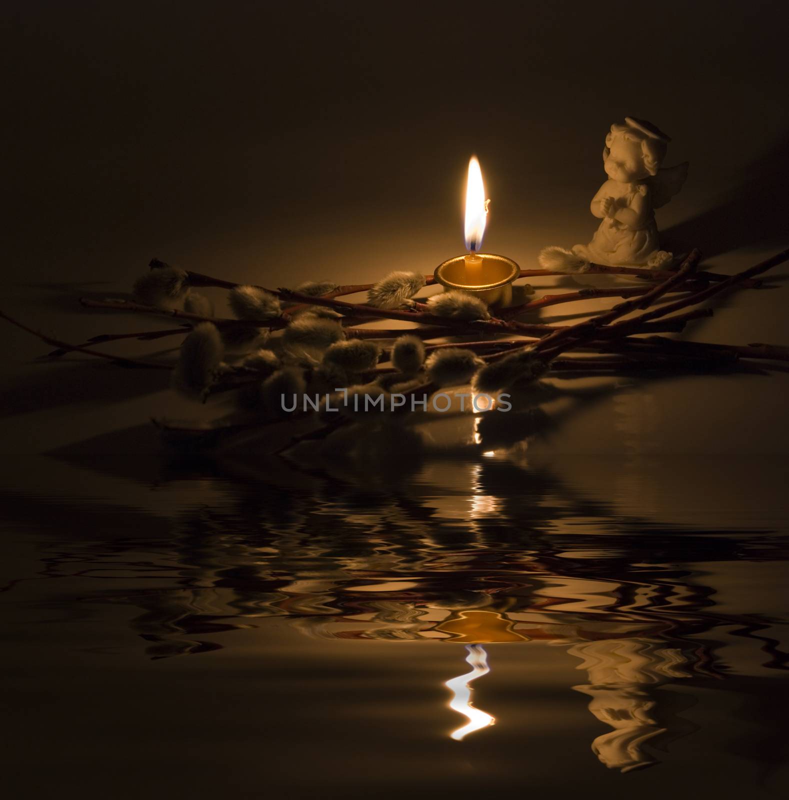 Angel, burning candle and willow twigs reflected in the water surface with small waves