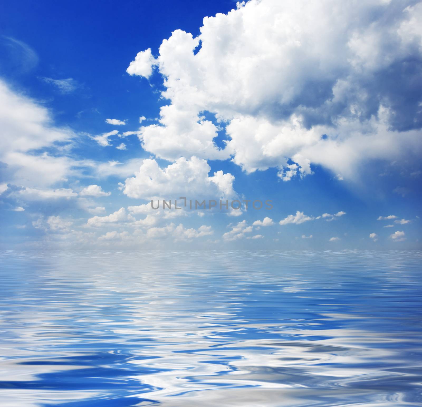 Blue sky with white clouds reflected in the water surface with small waves