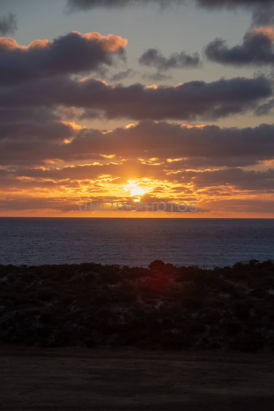 Sun shining through orange clouds during sunset at the coast of Geraldton, Australia by MXW_Stock