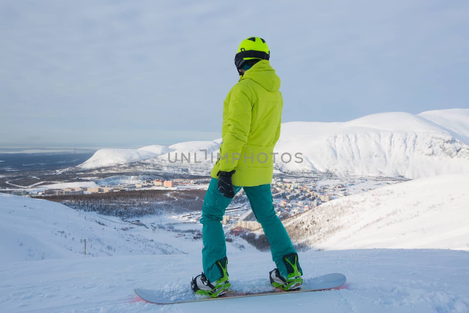 Kirovsk, Russia - Snowboarder on piste in high mountains on ski slope. Rear view. Winter snowboard and skiing concept. Khibiny Mountains, Kola Peninsula panoramic view in town