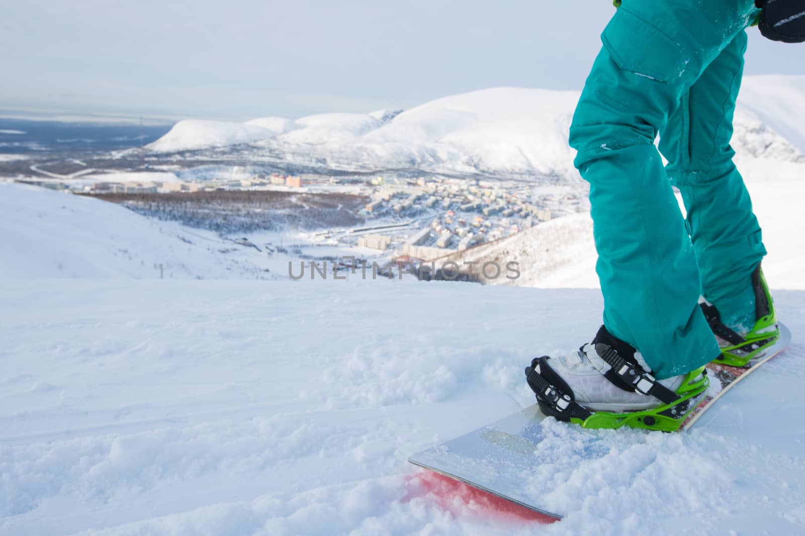 Kirovsk, Russia - Snowboarder on piste in high mountains on ski slope. Rear view. Winter snowboard and skiing concept. Khibiny Mountains, Kola Peninsula panoramic view in town
