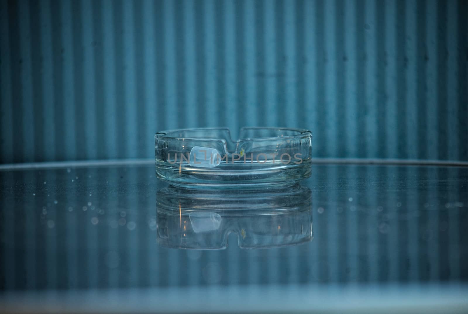 Glass ashtray on glass table in front of blue and white background