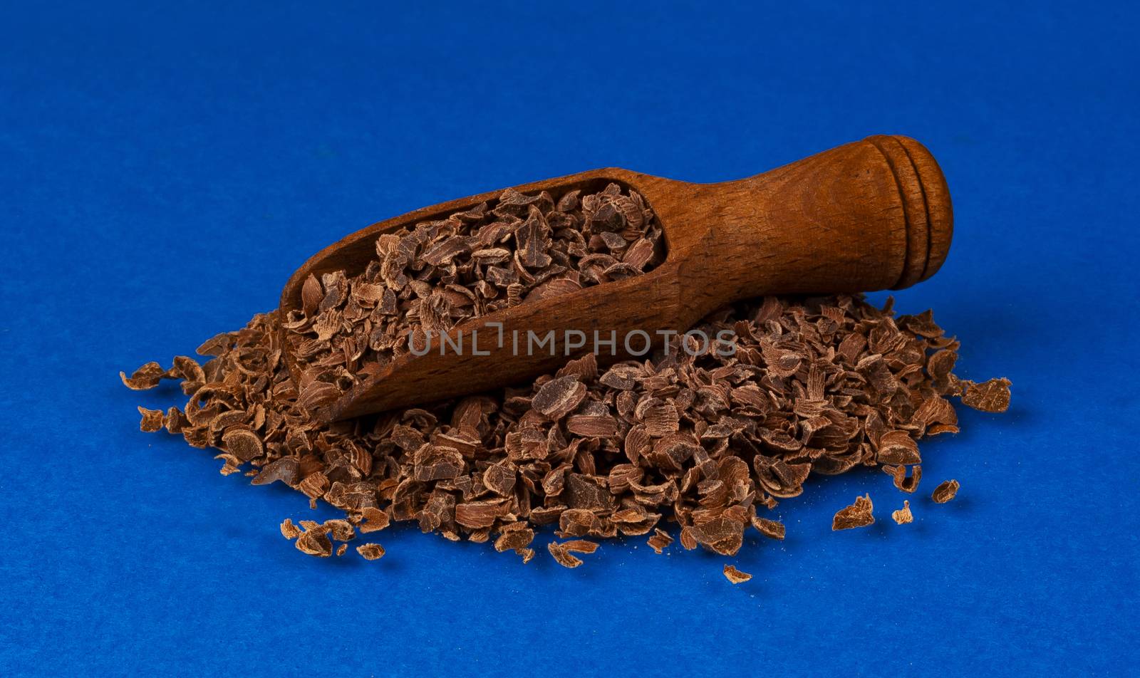 Grated chocolate. Pile of ground chocolate in wooden scoop isolated on blue color background with clipping path, closeup