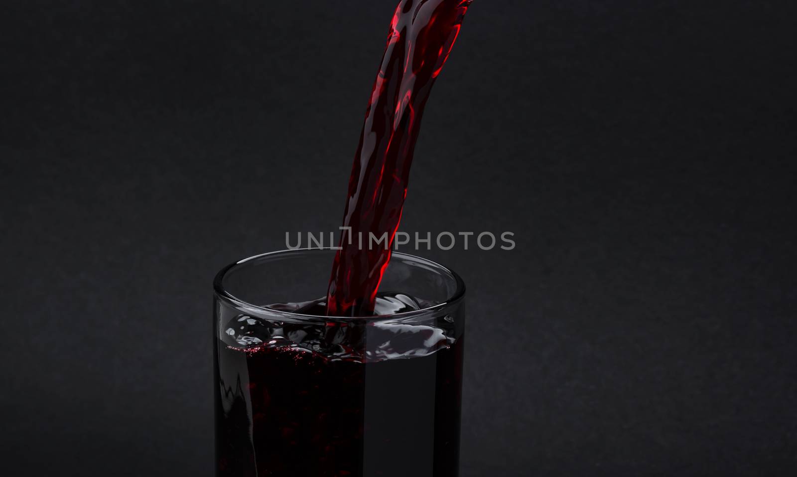 Cherry juice pouring into glass, isolated on black background, with copy space